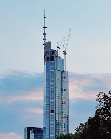 A sleek, modern skyscraper under construction against a clear blue sky, symbolizing growth and ambition.