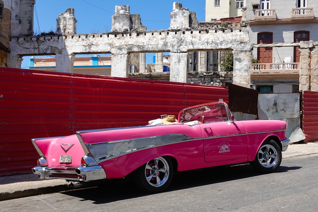 pink convertible car parked beside red building