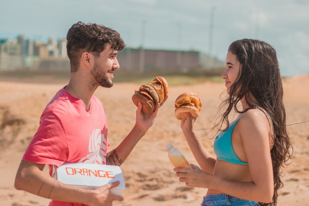 man in pink crew neck t-shirt holding bread with woman in blue bikini top