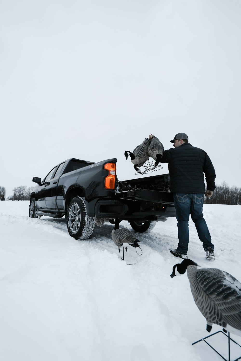 Hombre con chaqueta negra y jeans de mezclilla azules de pie junto a un SUV negro en suelo cubierto de nieve