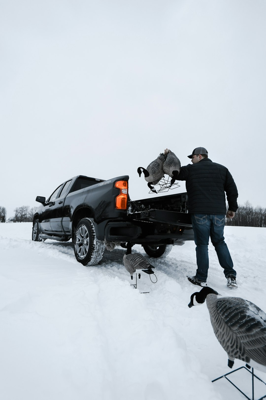 man in black jacket and blue denim jeans standing beside black suv on snow covered ground