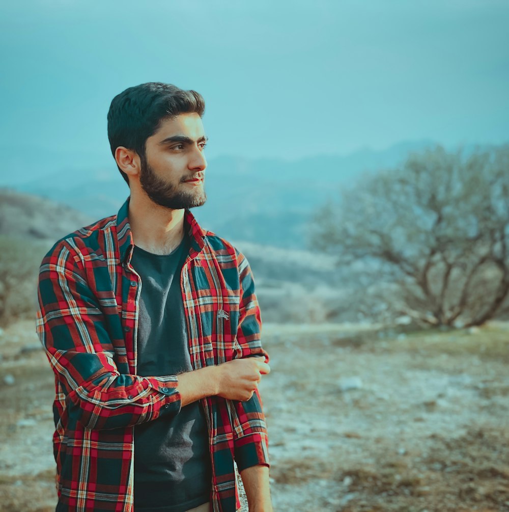 man in red and black plaid dress shirt standing on brown field during daytime