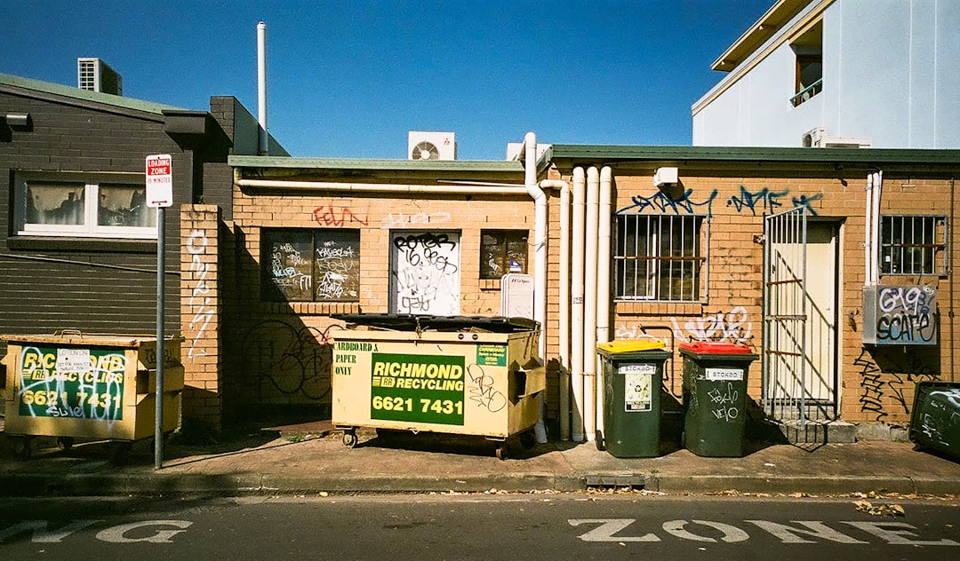 green trash bins beside brown brick building during daytime