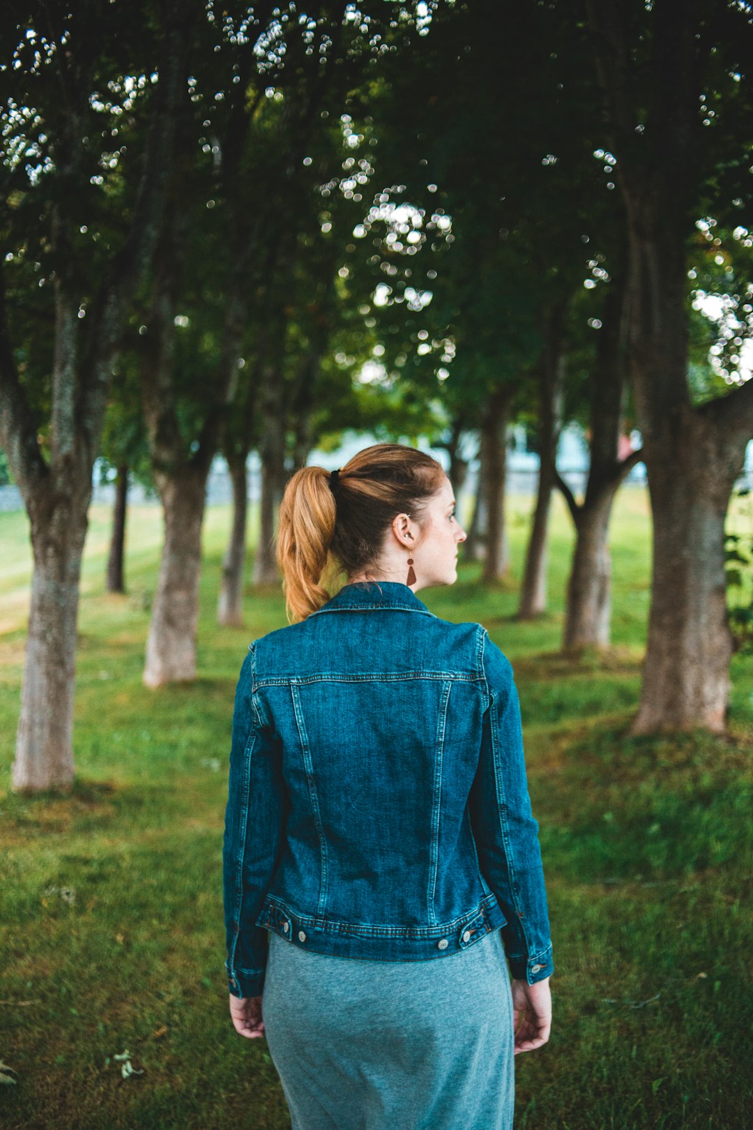 woman in blue denim jacket standing near trees during daytime