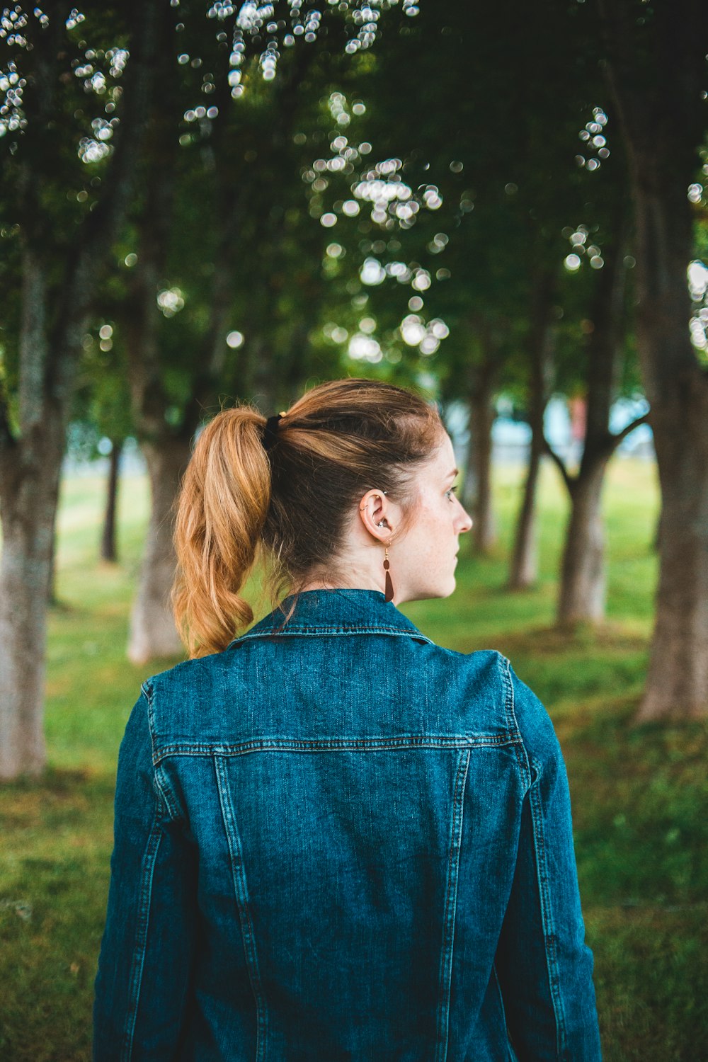 Frau in blauer Jeansjacke steht tagsüber in der Nähe von Bäumen