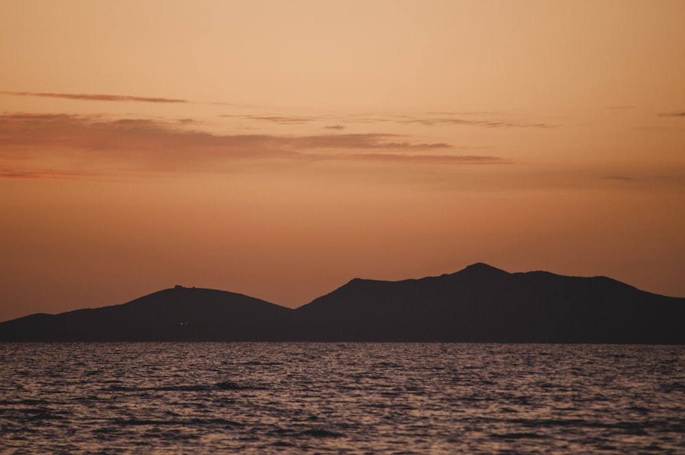 silhouette of mountain near body of water during sunset