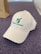 A white baseball cap with the words 'Voices of Autism' embroidered in green alongside a logo featuring a stylized person and airplane. The cap is placed on a textured, purple surface, with part of a brown paper bag visible in the background.