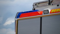 The image captures the side of a fire truck with vibrant red, blue, and yellow colors. The sky is cloudy, adding a dramatic backdrop to the scene. The truck has a distinctive emergency light bar and a compartmentalized appearance.