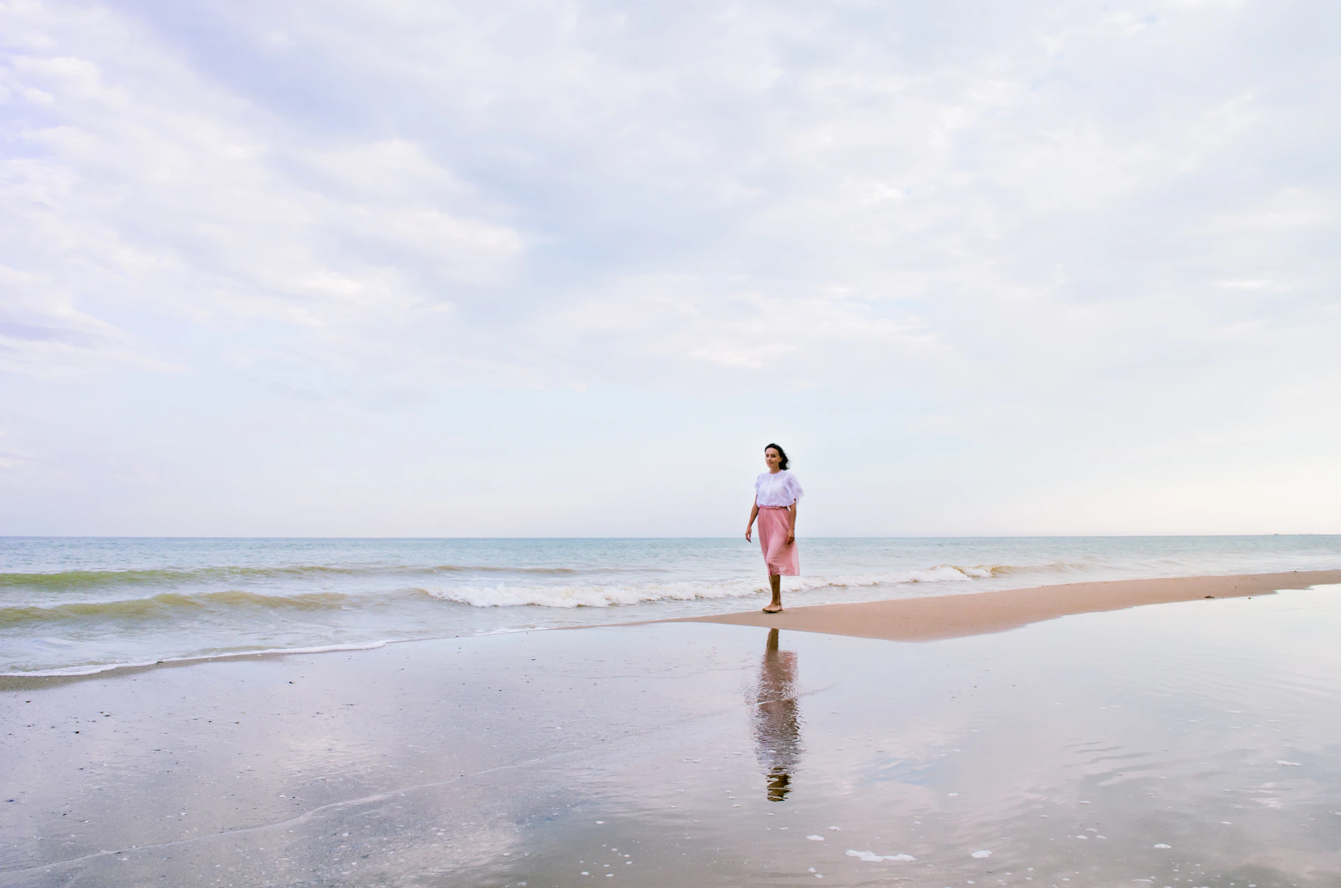 woman in white shirt and blue denim shorts walking on beach during daytime