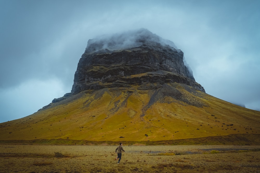 Persona che cammina sul campo marrone vicino alla montagna durante il giorno