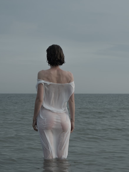 woman in white spaghetti strap dress standing on sea shore during daytime
