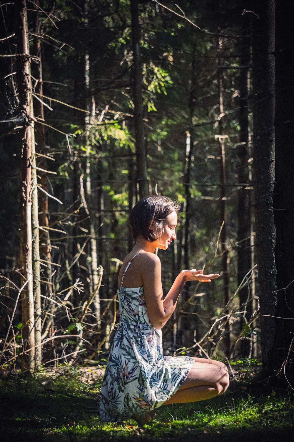 Mujer en vestido floral azul y blanco de tirantes de espagueti de pie en el bosque durante el día