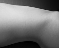 A monochrome photograph displays a minimalist view of a body part with smooth skin texture. The lighting creates subtle shadows, emphasizing the natural curves and contours.