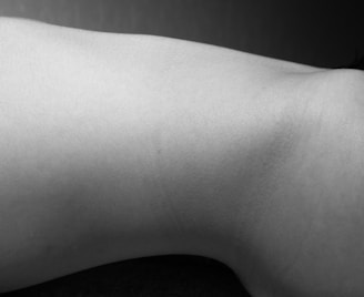 A monochrome photograph displays a minimalist view of a body part with smooth skin texture. The lighting creates subtle shadows, emphasizing the natural curves and contours.