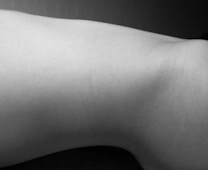 A monochrome photograph displays a minimalist view of a body part with smooth skin texture. The lighting creates subtle shadows, emphasizing the natural curves and contours.