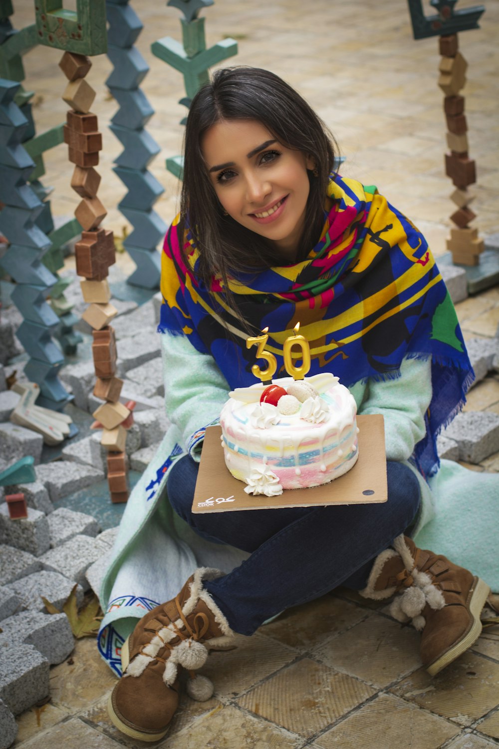 girl in black and yellow jacket sitting on blue and white textile with cake on lap