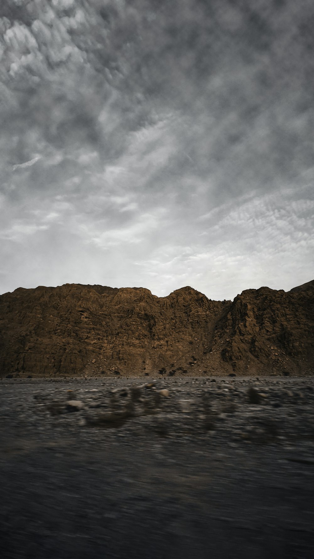 Brauner Berg in der Nähe von Gewässern unter bewölktem Himmel während des Tages