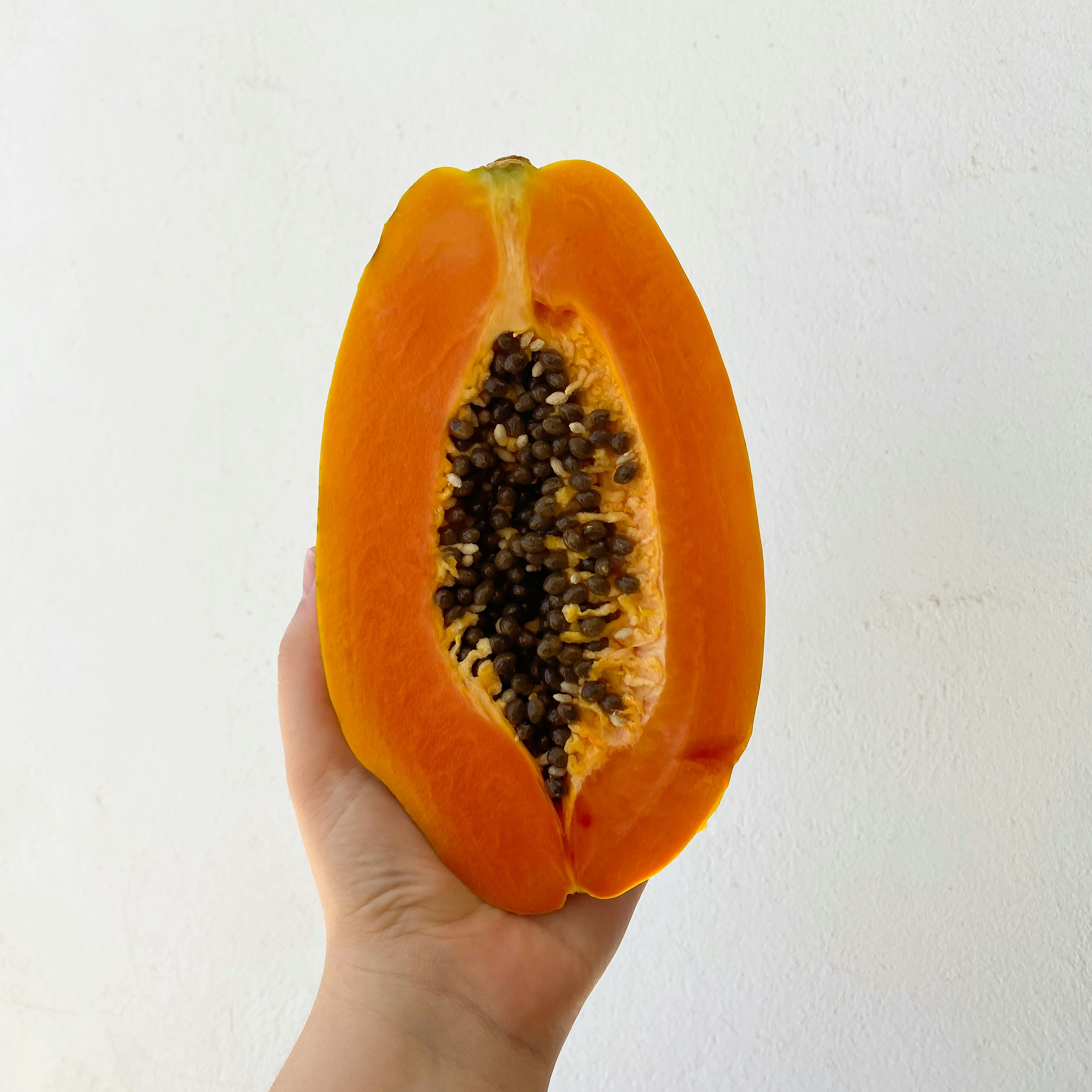 Halved ripe papaya showing orange flesh and black seeds on a bright white surface
