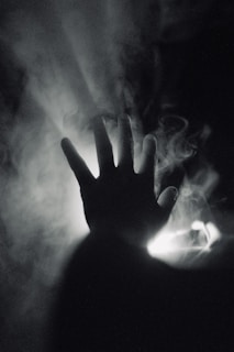 Silhouetted hands reaching out in front of a smoky, backlit scene.