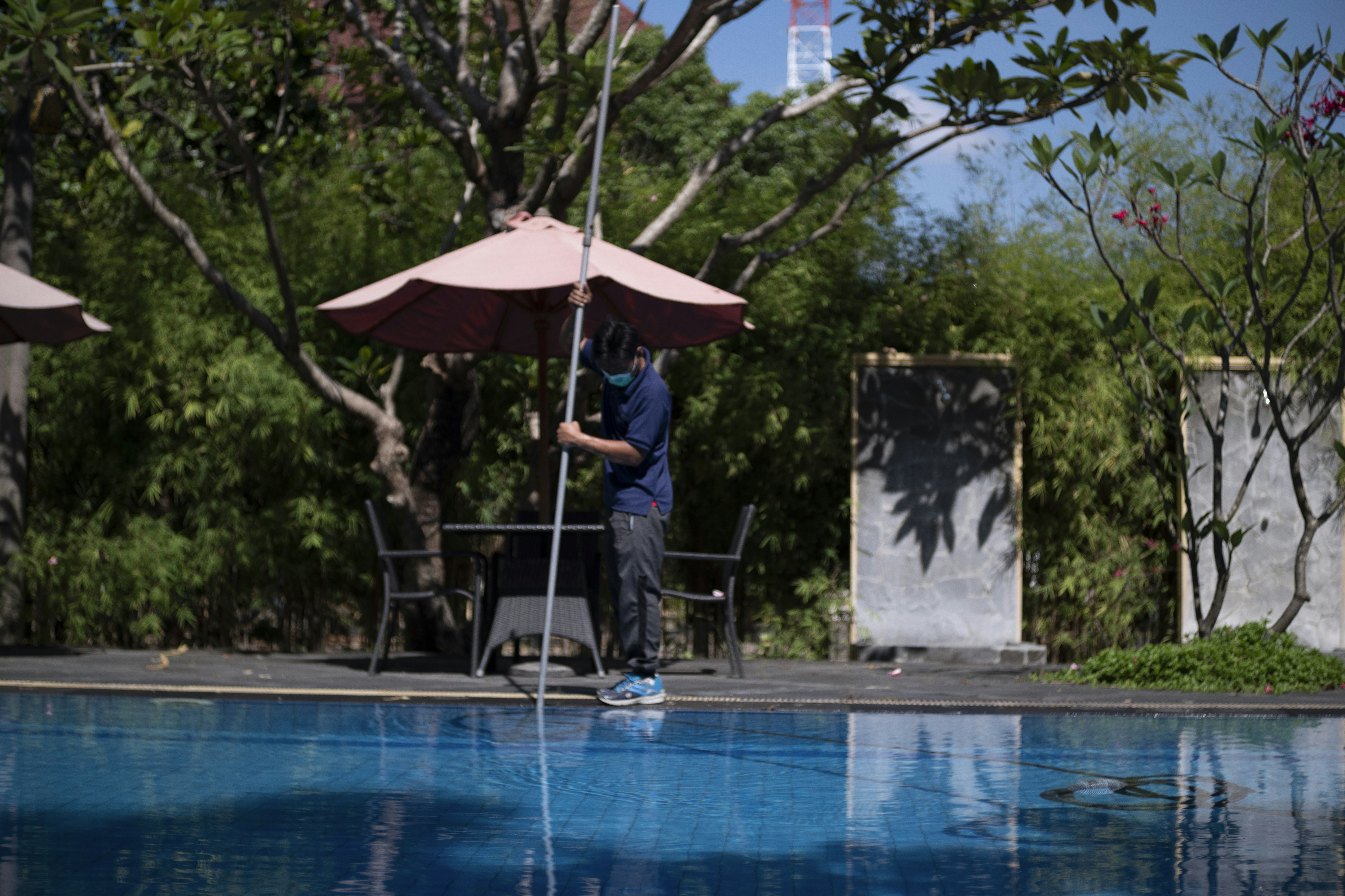 woman in pink shirt and blue denim jeans standing near swimming pool during daytime