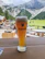 A frothy glass of Swiss beer on a rustic wooden bar counter with a football match playing in the background.