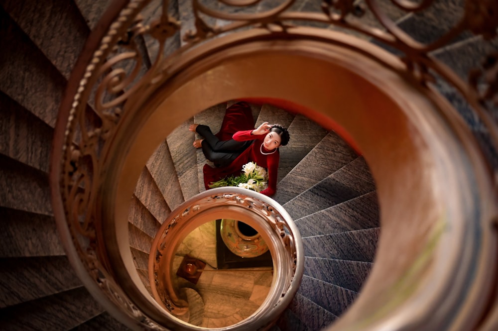 person in green jacket and red pants climbing on brown spiral staircase