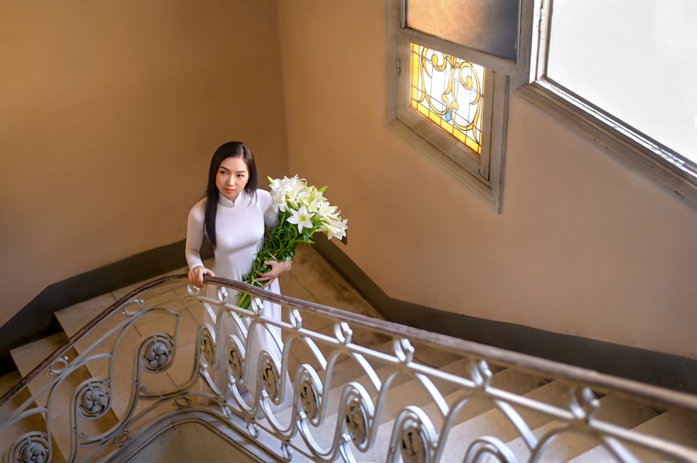 woman in white sleeveless dress holding bouquet of flowers standing on staircase