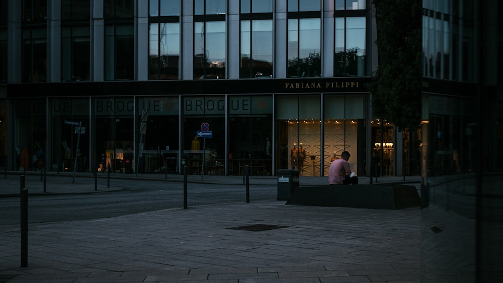 Mann in schwarzer Jacke sitzt tagsüber auf der Bank vor dem Gebäude