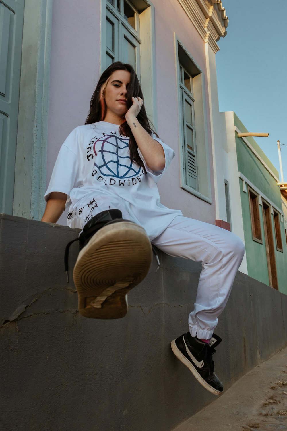woman in white and black crew neck t-shirt and white pants sitting on brown wooden