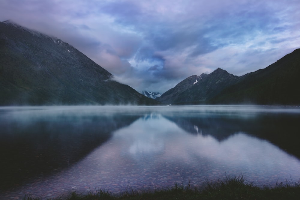 lake near mountain under white clouds and blue sky during daytime