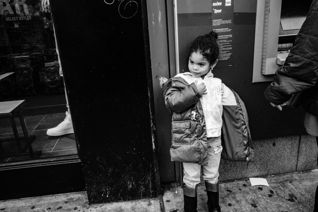 grayscale photo of boy in jacket and pants standing beside door