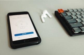 A smartphone with a meeting application open, placed on a light gray surface. Next to it, an earbud and a mechanical keyboard are visible.