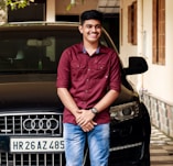 man in red button up shirt and blue denim jeans sitting on black mercedes benz car