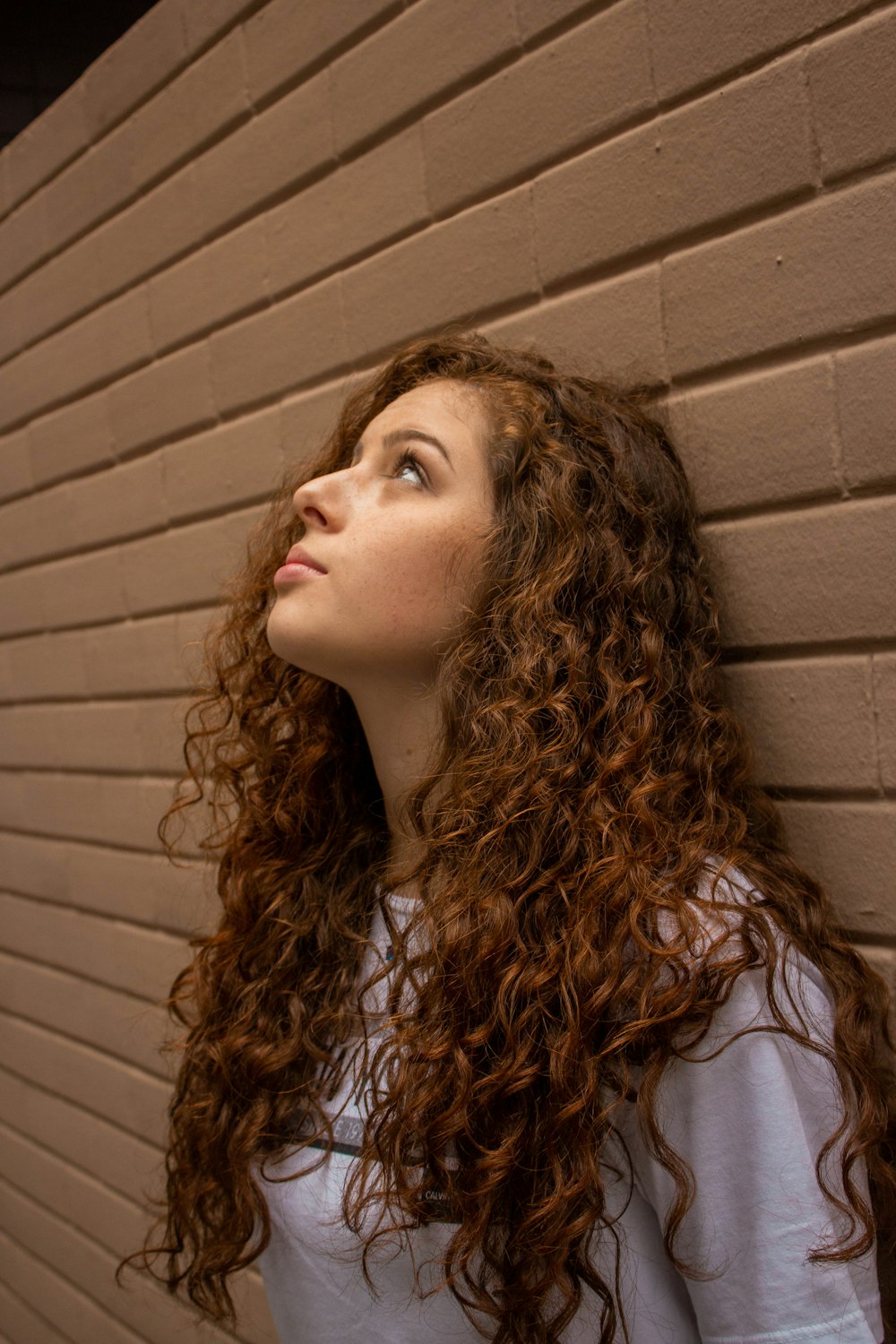 woman in white shirt standing beside brown wall