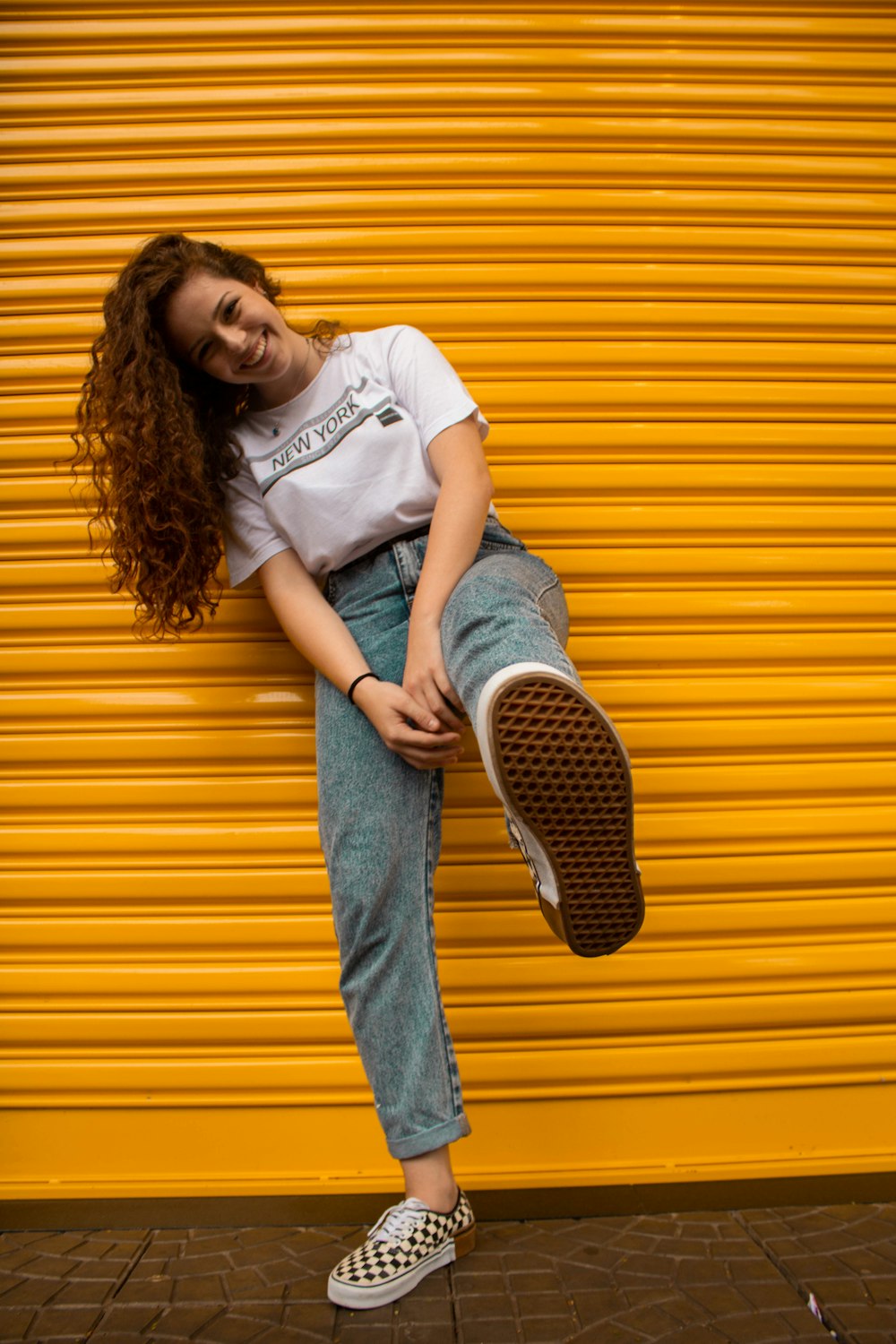 woman in white crew neck t-shirt and blue denim jeans leaning on yellow wall