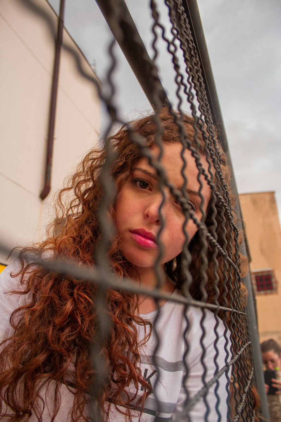 woman in white shirt leaning on brown metal fence during daytime