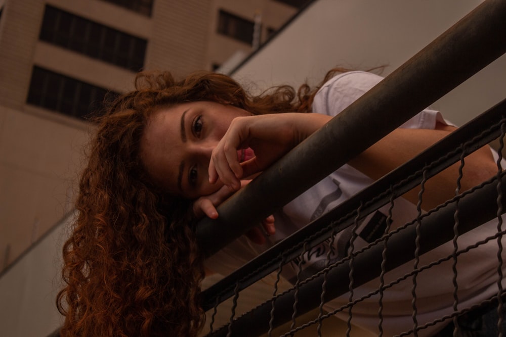 girl in white shirt leaning on gray metal fence