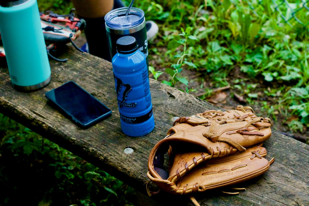 blue and black tumbler beside brown leather bag on brown wooden table