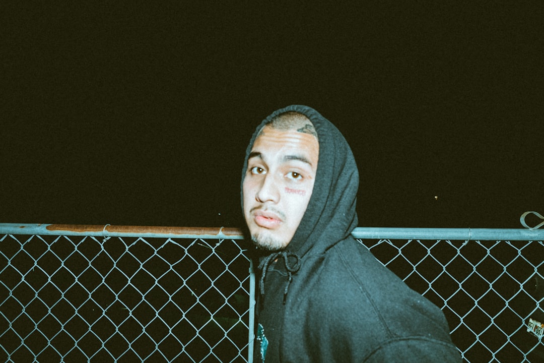 man in gray hoodie standing beside gray metal fence