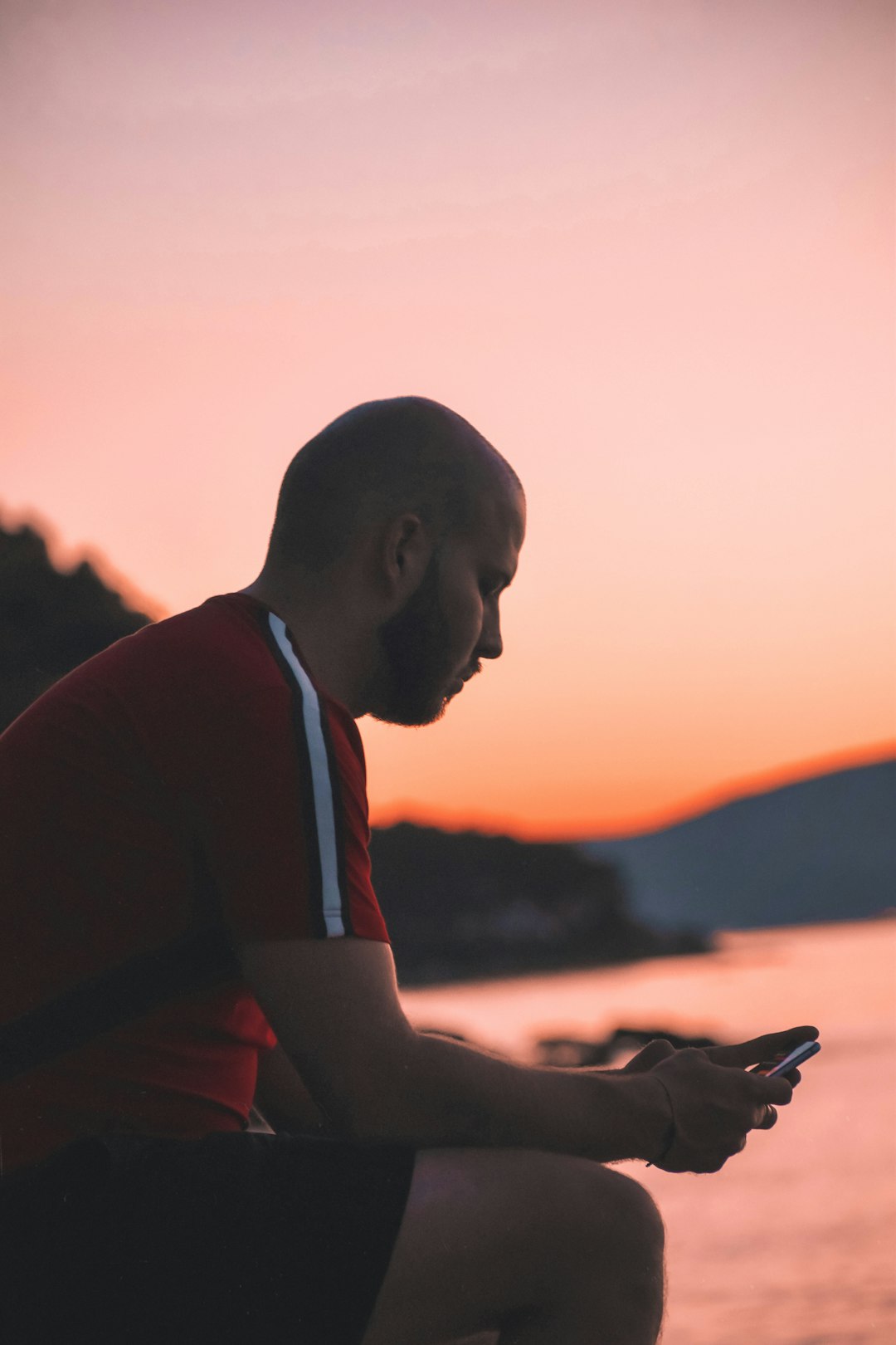 man in red and black shirt holding smartphone during sunset