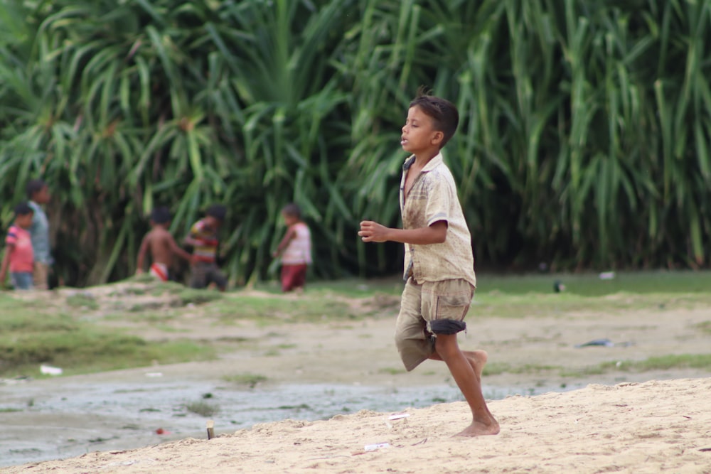 boy in white t-shirt and brown shorts running on brown sand during daytime