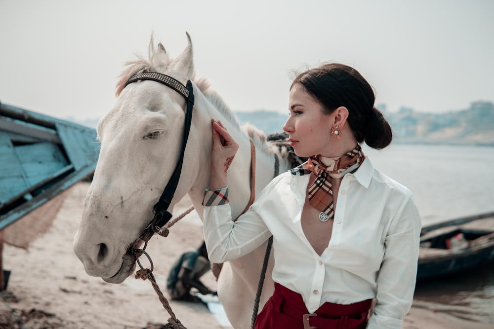woman in white button up shirt standing beside white horse during daytime