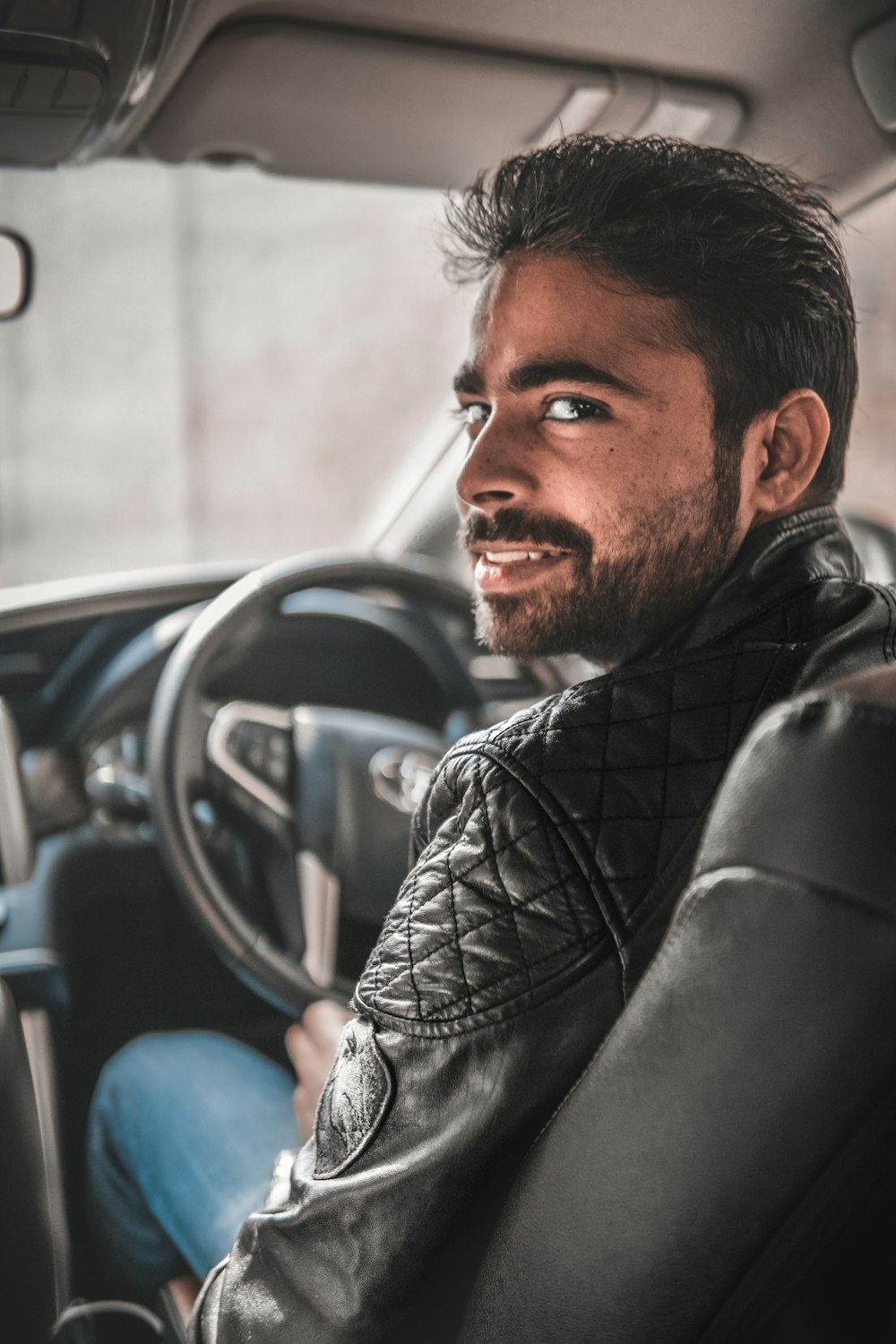 hombre con chaqueta de cuero negro sentado en un asiento de automóvil azul