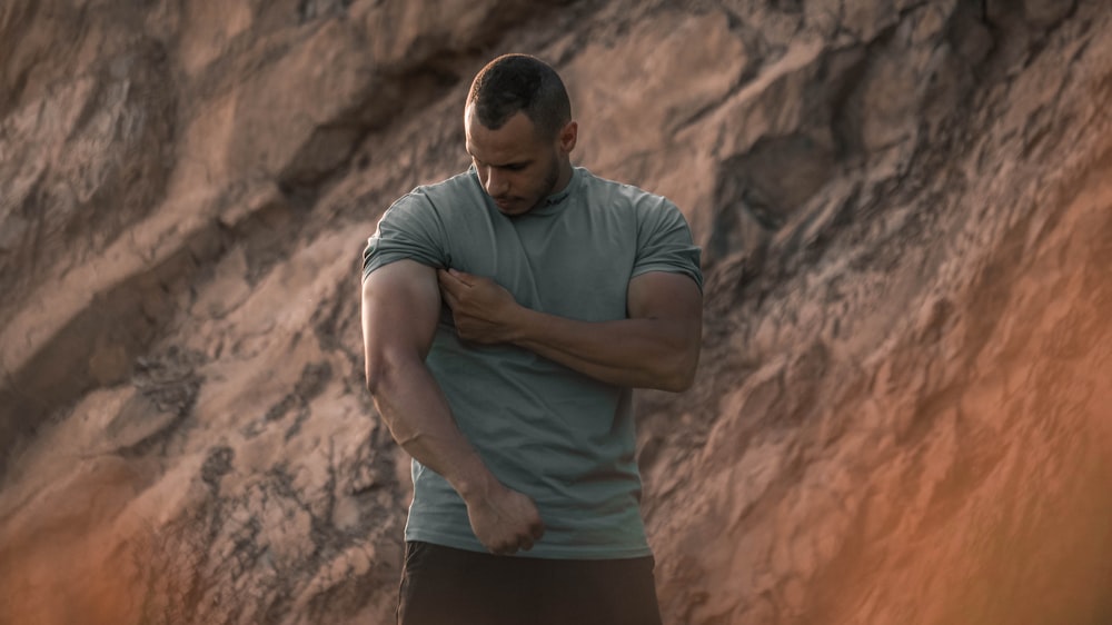 man in gray polo shirt and black shorts standing near brown rock formation during daytime