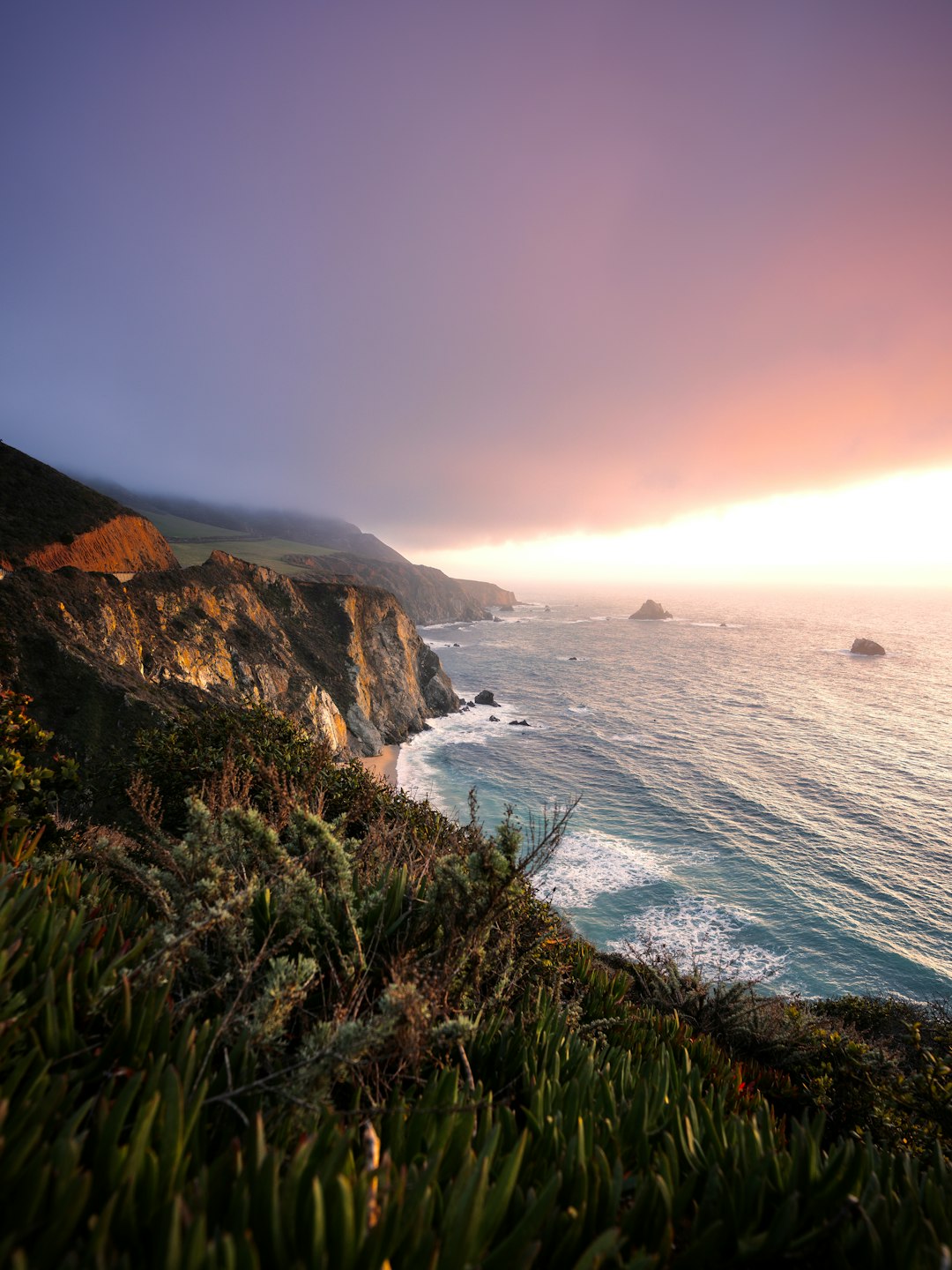 green grass on brown rocky mountain beside blue sea under blue sky during daytime