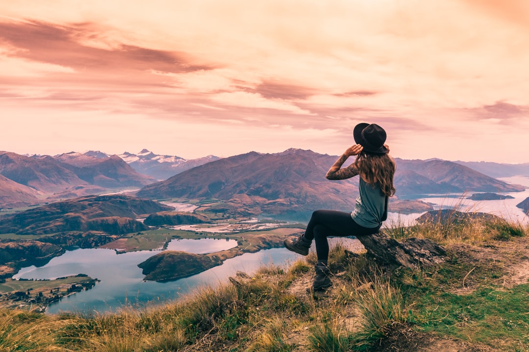 woman in black shirt and black pants sitting on rock near lake during daytime