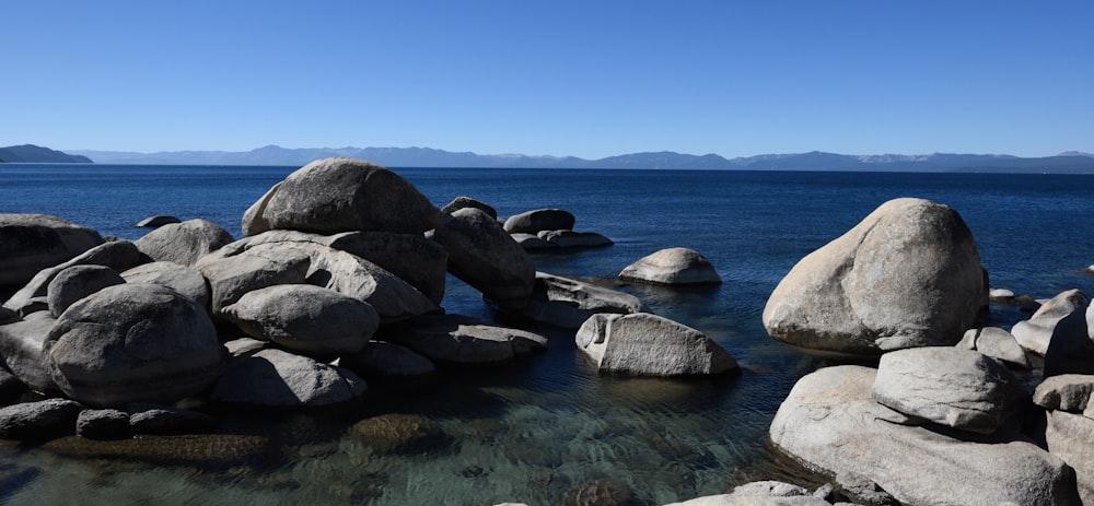 black rocks on body of water under blue sky during daytime