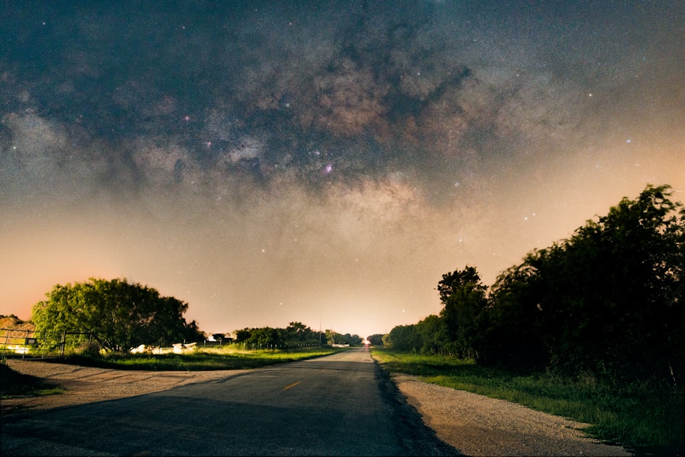 gray asphalt road between green trees under blue sky during night time