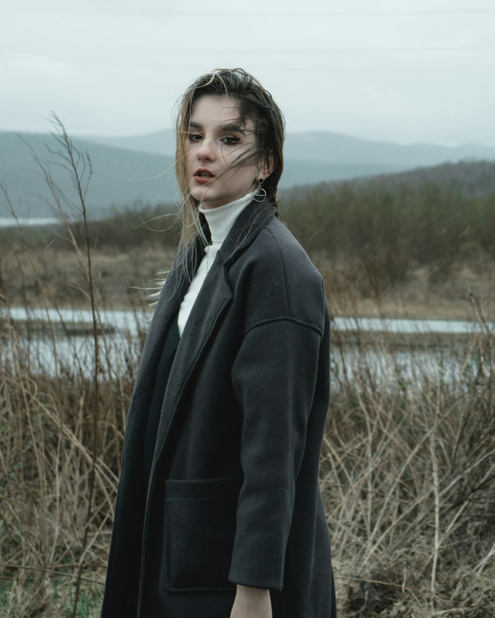 woman in black blazer standing on grass field near lake during daytime