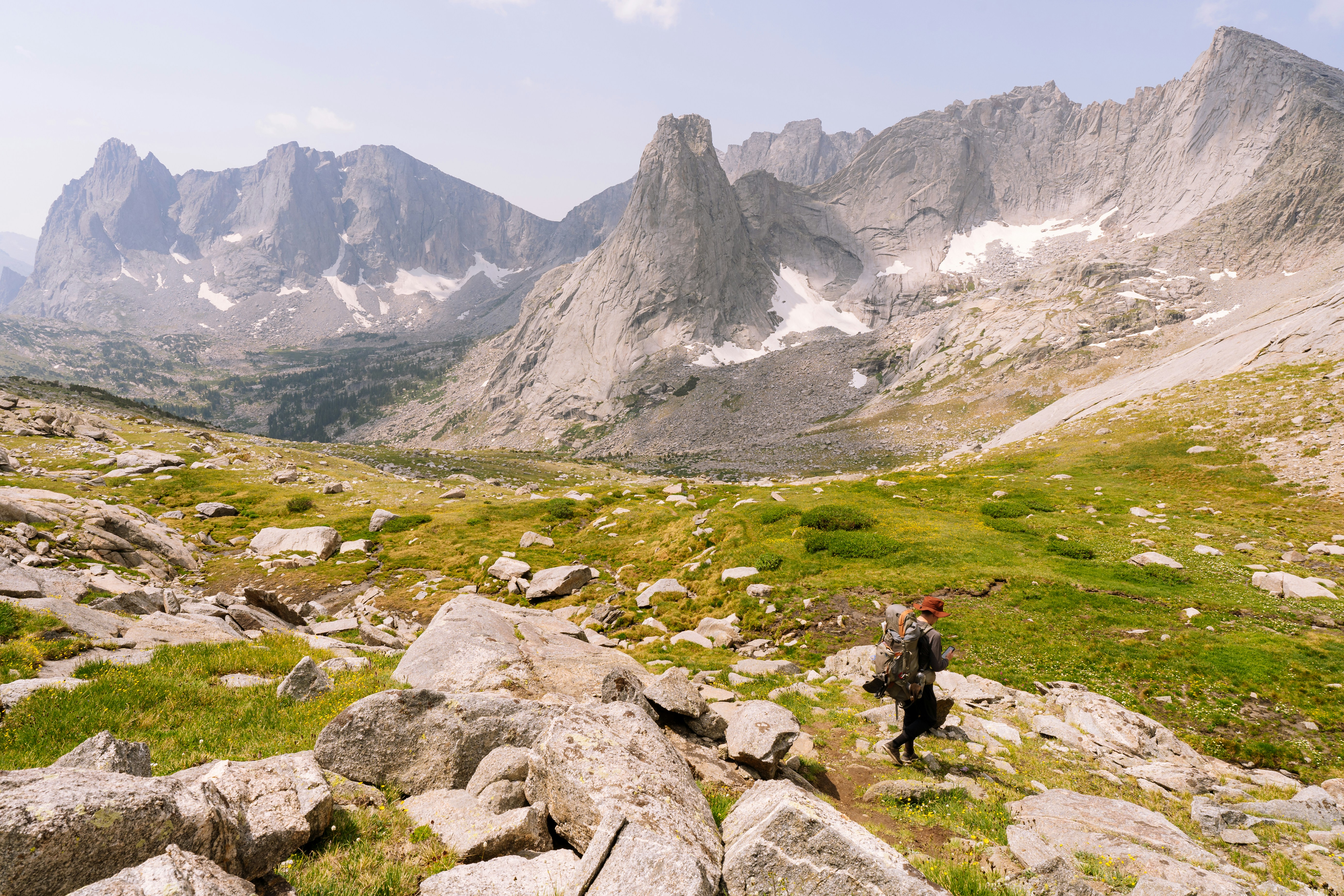 person in a black jacket sitting on a rock near a gray rocky mountain during the day